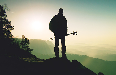 Tourist with poles in hand. Sunny spring landscape rocky summit. Hiker guide on the summit with poles in hand and heavy backpackkの写真素材