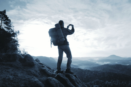 Hiker in sporty suit stand on peak in rock and watching over the misty and foggy morning valley to Sunの写真素材