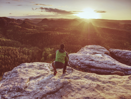 Professional photographer stay with tripod on cliff and thinking.  Foggy landscape spring orange pink misty sunrise in beautiful valley below.の写真素材