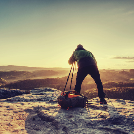 Picture shooting process in nature. Artist holding camera on tripod and pointing with view finder directing into rising sunの写真素材