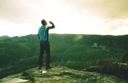 Man on a cliff edge on the top of mountain with gorgeous view and drink waterの写真素材