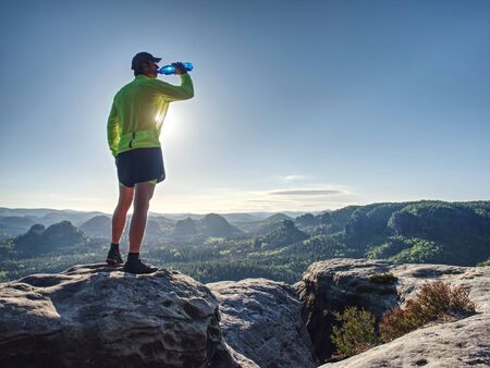 Fit runner in sport suit drinking the water from sport bottle with relax action in deep forest in morning timeの写真素材