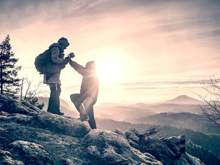 Tourists couple stay on summit and takes memory picture with camera on tripod.  Hiker and photo enthusiast stay with tripod on cliff and thinking. Dreamy fogy landscapeの写真素材