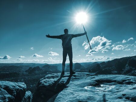 Tourist boy with backpack and sticks in foggy mountain range standing on rocky top on bright blue morning sky background.の写真素材