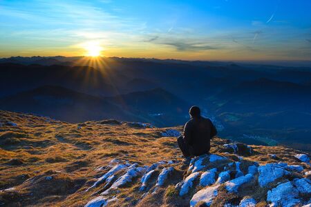Man in black outdoor clothes sit on cracked rocky summit in Alps watchin amazing sunsetの写真素材
