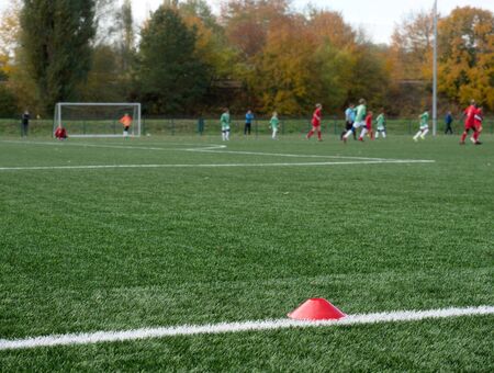 Selective focus to arker cones used for soccer training on green artificial turf with blurry kid...