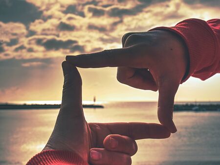 Hands making finger shape gesture, hand hold sun above stony fisherman pier, Mallorka island.の写真素材