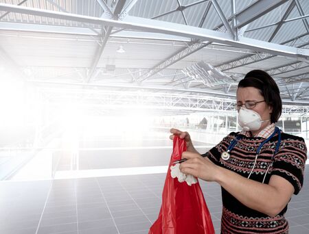 Woman with face breathing protection mask put paper waste into plastic bag.  Airport building.の写真素材