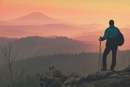 Man walk to Camp by trekking rocky route. Backpacker carrying Backpacks and using trekking poles and enjoying far valley viewの写真素材