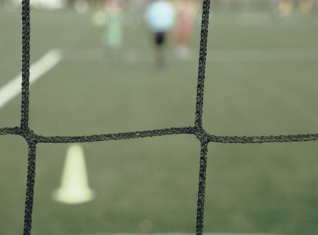 View through football gate net during a football mach. Goal keeper wait in front of gate line
