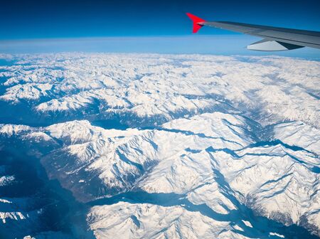 Airplane wing with red winglet float in clear air over snowy winter Swiss Alps.の写真素材