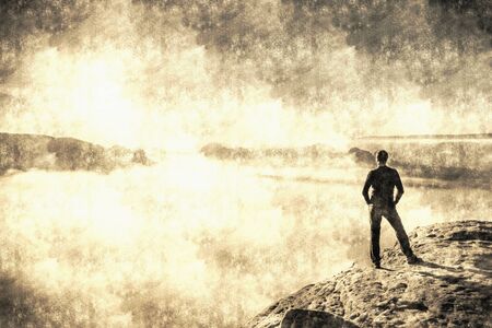 Sporty man on mountain peak looking on mountain valley with low mist at colorful sunset in autumn. Calotype filter. Old photo style.の写真素材