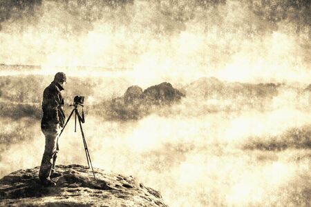 Landscape with a man in top of a peak taking photos with his camera on the stick at sunset.  Calotype filter. Old photo style.の写真素材