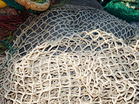 White dry fishing net with floats on pavement at anchored fishing boat. Empty net at fish market
