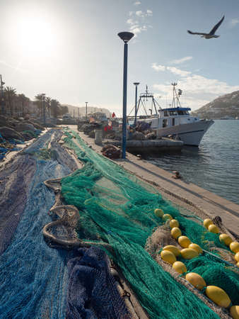 Pile of different fishing nets used for offshore fishing and trawling laying on the docks. Fishing boat waits for next shiftの写真素材