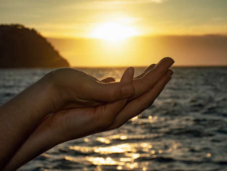 The sun on female hand. Silhouette of hand holding sun above seaの写真素材