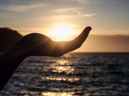 Touch the sun above the sea in the morning, Summer holiday at sea beach. Pick up the sun by hand. Yellow light with cold air in winter, Flare from sunriseの写真素材
