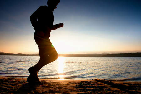 Running man on beach. Sportsman run in baseball cap, jogging guy during the sunrise above sandy...