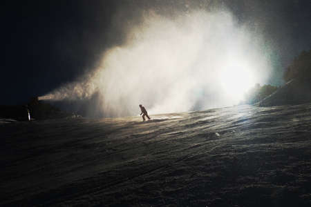 Snowmaking on slope. Skier near a snow cannon making fresch powder snow. Mountain ski resort and winter calm mountain landscape.の写真素材