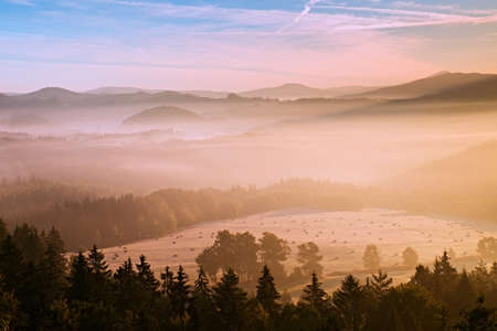 Pink daybreak in hilly landcape. Autumn misty morning in a beautiful hills. Peaks of hills are sticking out from fogの写真素材