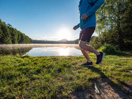 Athlete at the lake running against sunrise and colorful nature.の写真素材