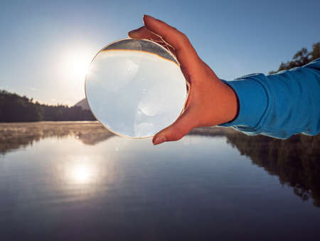 Hand hold glass lens or ball uniquely reflects summer lake scene with sunset.の写真素材