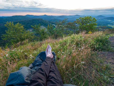 Hikers barefoot legs lay evening on sleeping bag. Tourist prepare bivouac on his trail.