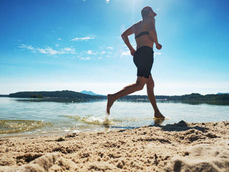 Shirtless fitness man exercising in outdoor training on the beach. Muscular man is running in water along beach, holidays conceptの写真素材