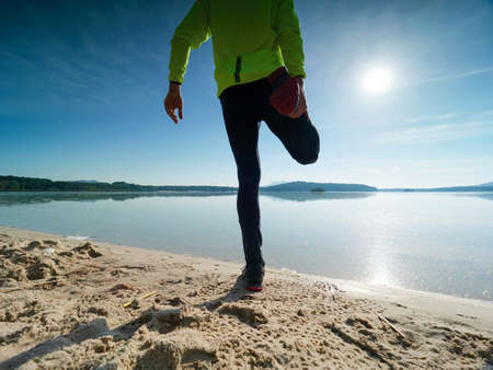 Tall slim man doing stretching on the beach on a sunny morning. Body stretching before doing sports.