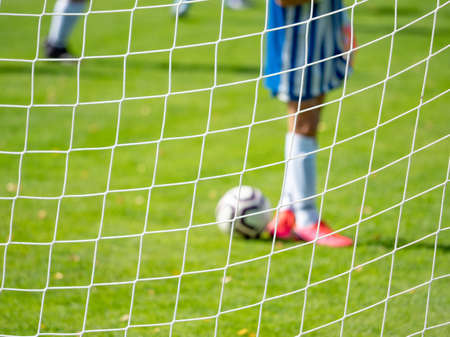 Young football goalkeeper in playground. Out of focus. View through the football gate net.の写真素材