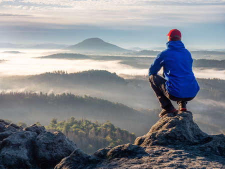 Nature adventure. Hiker sit on the rock and watch over the misty morning valley to rising sun at horizon.の写真素材