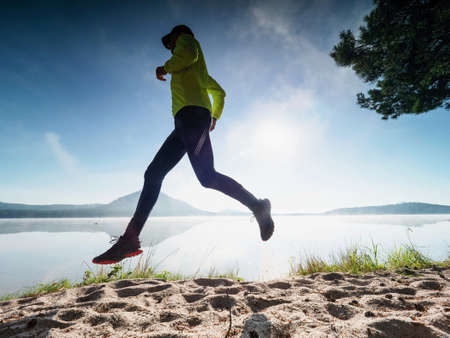 Slim man jogging on the beach early morning. Runner in yellow black running suit during run along lake.の写真素材