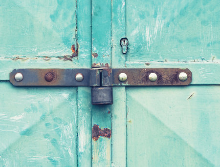 Old rusty lock latch on the metal door. Obsolete cracked painted surface with weathering marks.の写真素材