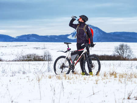 Extreme cyclist stopped the winter training and drinks a refreshing drink from a thermos. Challenging winter terrain with his white fatbike.の写真素材