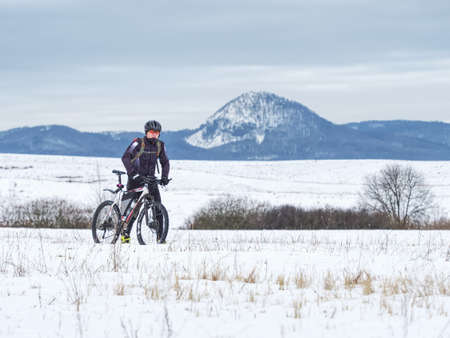 Biker is pushing bike in deep snow alone. Mtb rider lost the road under snow. Cold winter day, hills at horizonの写真素材