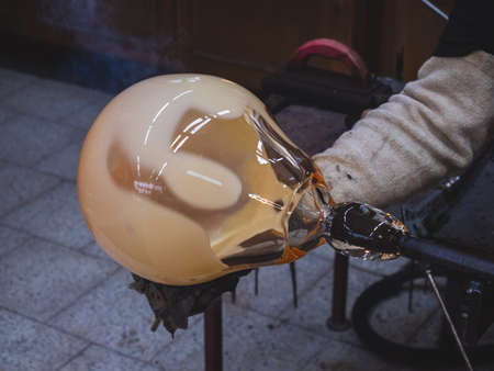 Man artists hands working on a Blown Glass Piece. Shaping glass bowl with wet tool. Rounding the hot glassの写真素材