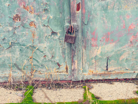 Obsolete green gate or door with padlock. Cracked painted surface with rusty spots and obsolete paint scales.の写真素材