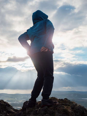 Cheerful boy is grimacing on top of the mountain where he climbed. View of the autumn landscape.