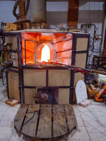 Shining glass blowing furnace at work. Gas kiln in glass design studio, manual production of glass...