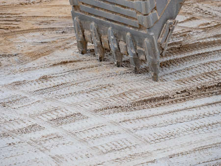 Excavator Loader standing in sandpit with pulled down bucket over trails of tracked trucksの写真素材