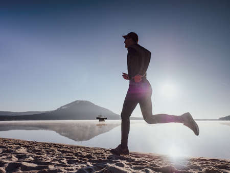 Full length of healthy man running and sprinting outdoors. Male runner. Man running on the beach at sunset.の写真素材