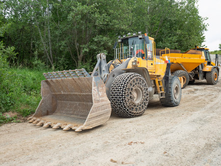 Heavy loader bulldozer bucket. Tractor loader with protective wheel chains on tires waits at the sandpitの写真素材