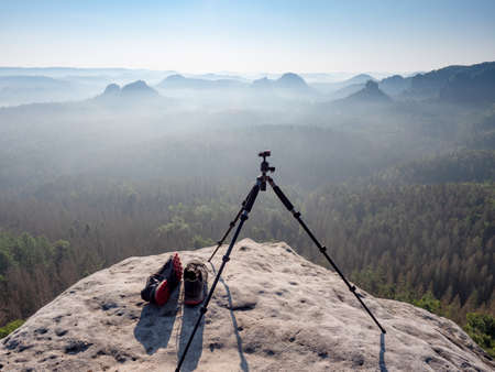 Modern professional travel tripod and black red sneakers on mountain summit. Hiking and takes photos in pure nature.の写真素材