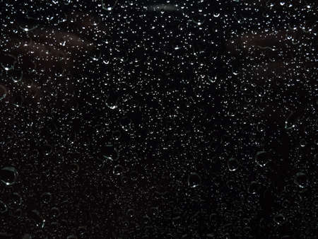 Rain droplets running down on a window glass, abstract backlight backgroundの写真素材