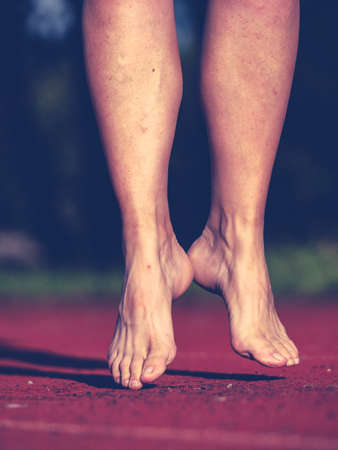 Stretching and warm up bouncing before a training run on the stadium oval. The body of a middle aged womanの写真素材