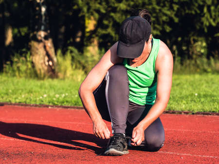 Female asian runner in green singlet stopped for lacing her sneakers. Health and sport conceptの写真素材