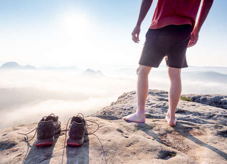 Middle age healthy male body with naked legs on mountain peak rock. Satisfy hiker enjoy view. Tall man on rocky cliff watching down to landscape.の写真素材