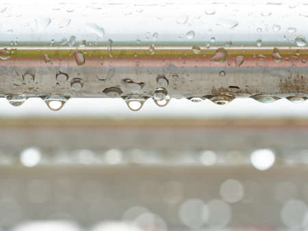 Stainless steel pipe of handrail in detail. Morning rain drops hanging and shining against gray skyの写真素材