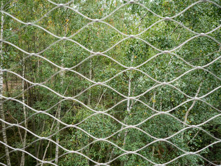 Modern stainless wire chainlink fence against green forest landscape. Secure wire fence at the borerの写真素材