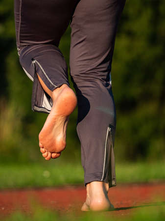 Bare feet woman stretching legs and preparing to run on the red floor at stadium. Regular fit training of middle age woman.の写真素材